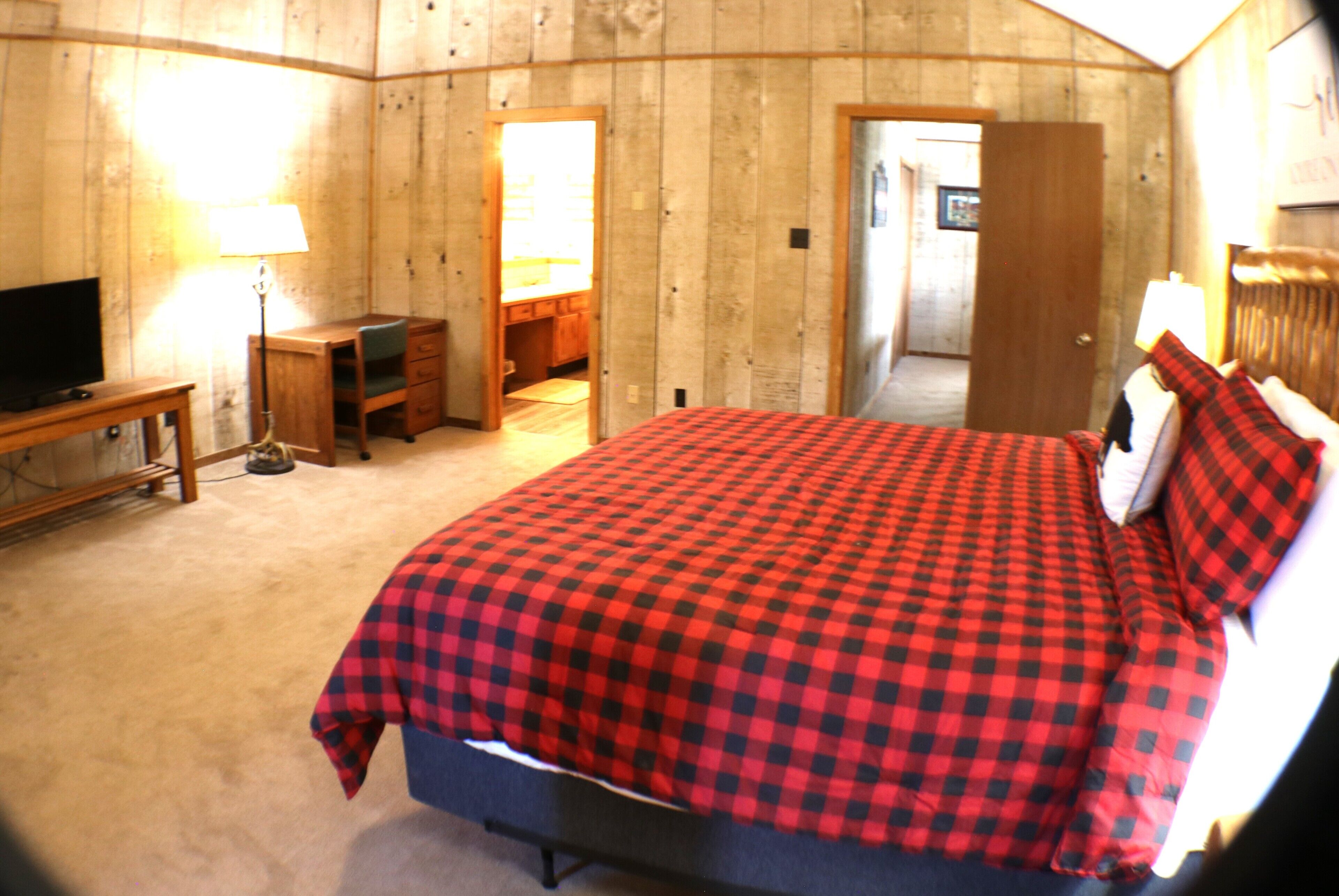 A bedroom with a checkered bedspread, a television, a desk, and a lamp.