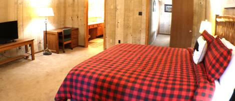 A bedroom with a checkered bedspread, a television, a desk, and a lamp.