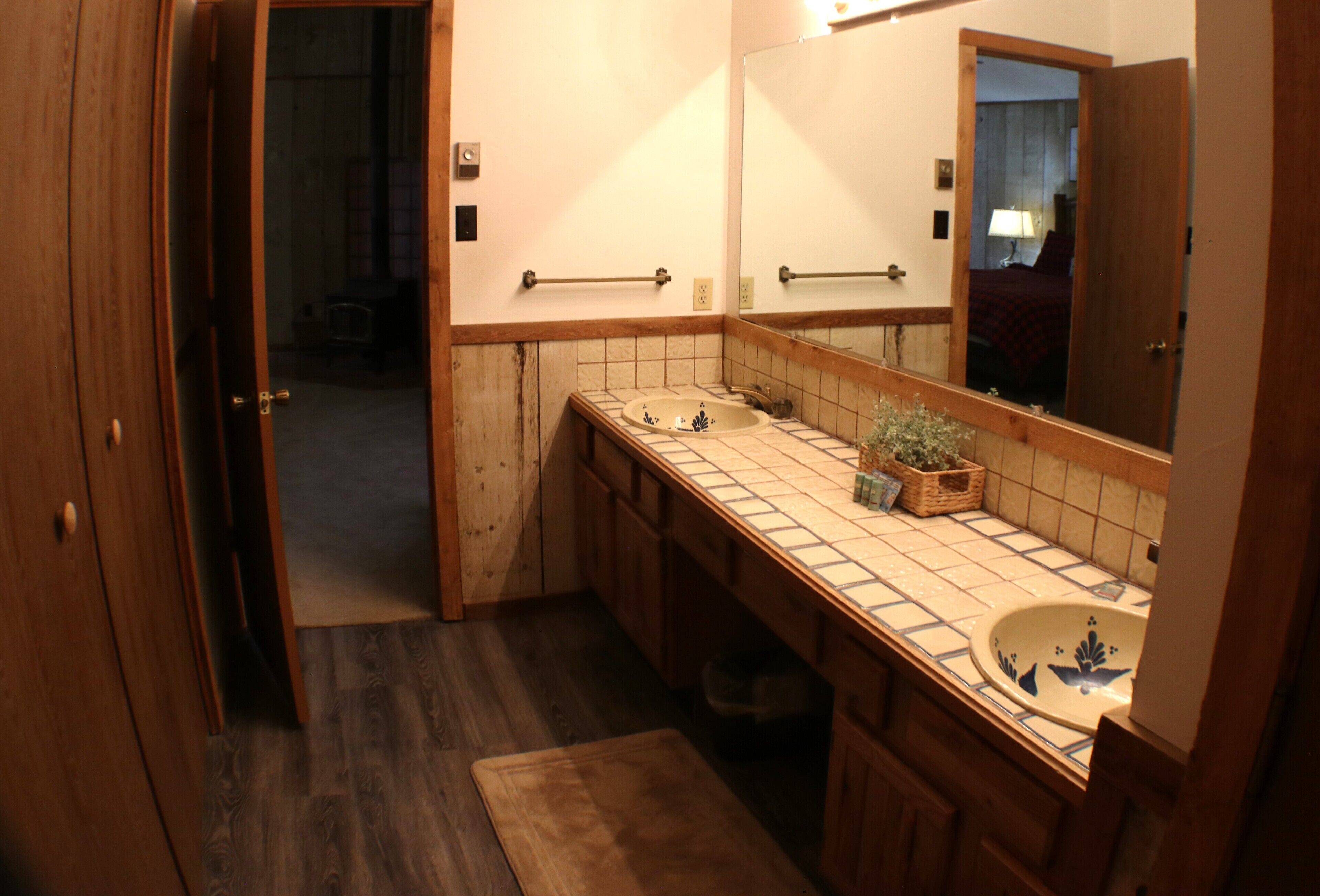 Un baño con tocador de madera, un lavamanos, un espejo y una planta pequeña en la encimera.