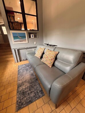 A grey leather sofa with patterned cushions, a grey rug, and a framed picture of a bird on the wall. - Belmont King Studio - Walk Everywhere - Pet Friendly (Pensacola)