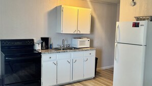Pieni, käytännöllinen keittiö, jossa on valkoiset kaapit, musta liesi, valkoinen jääkaappi ja mikroaaltouuni.