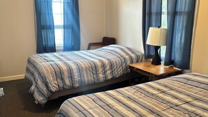 Hotellihuone, jossa on kaksi sänkyä, pieni pöytä, tuoli ja lamppu.