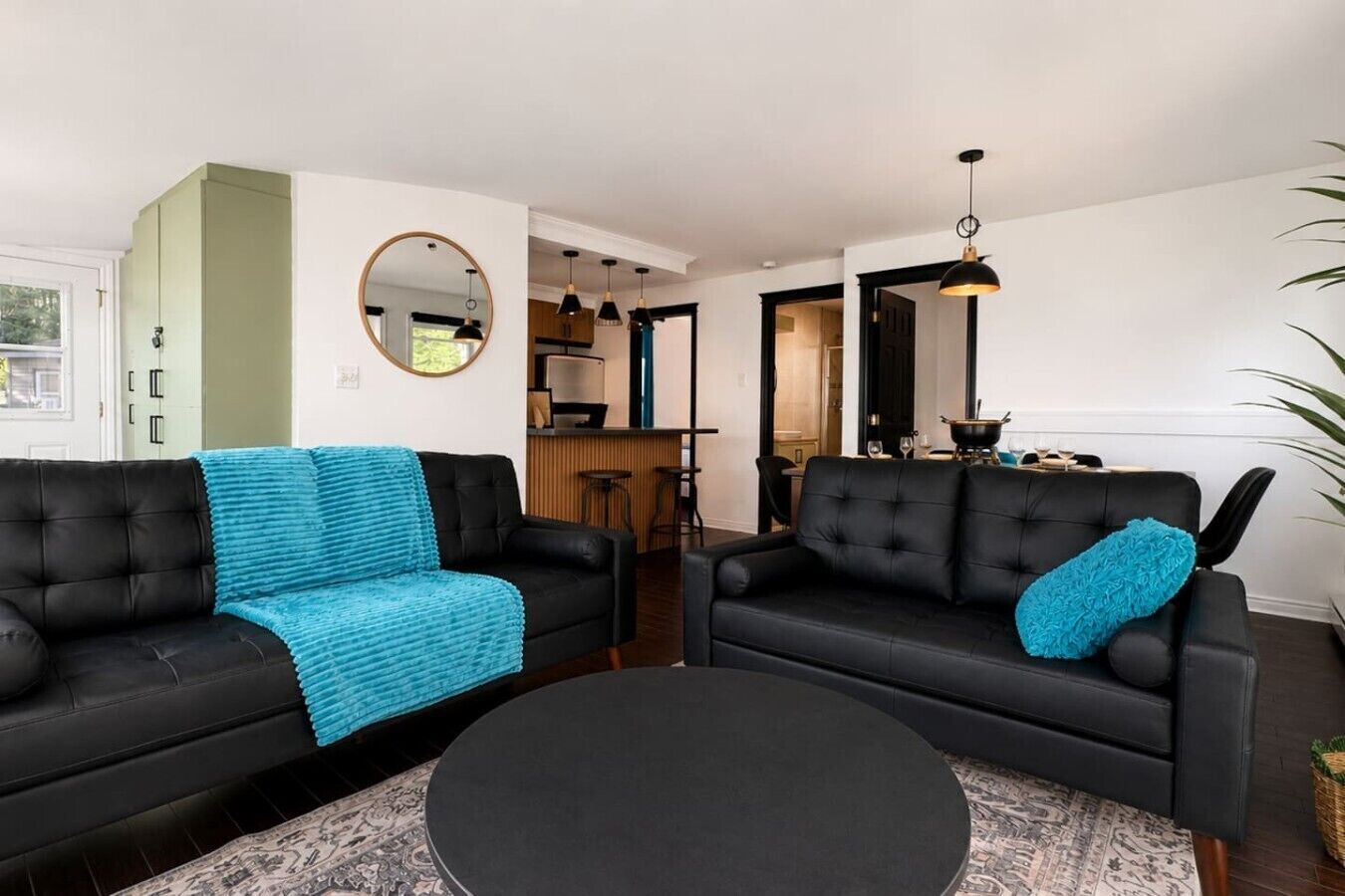 Een woonkamer met twee zwarte banken, een ronde salontafel, en een keuken op de achtergrond.