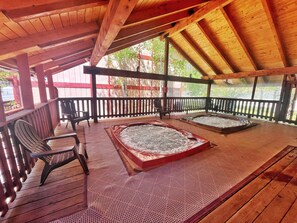 Eine Holzterrasse mit zwei Whirlpools, einer Holzbank und einem Geländer.