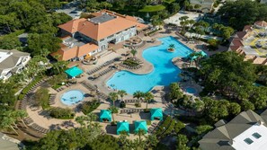Eine Luftaufnahme eines Resorts mit mehreren Schwimmbecken, einem großen Gebäude mit rotem Dach und umliegenden Palmen.