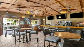 Eine Bar mit verschiedenen Sitzgelegenheiten, einer Theke mit einer Auswahl an Flaschen und einer Decke mit gewebtem Muster und hängenden Lampen.
