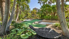 Ein tropischer Garten mit Swimmingpool, Palmen und einer großen Schildkröten-Skulptur.