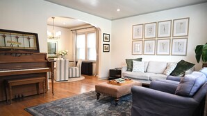 Ein Wohnzimmer mit Klavier, Sofa, Couchtisch und gerahmten Blumenbildern an der Wand.