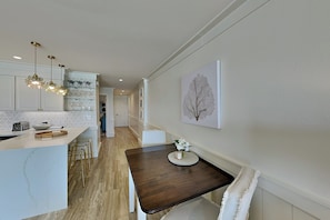 Une cuisine moderne dotée d’un plan de travail en marbre, de luminaires suspendus et d’un coin repas avec une table en bois foncé et des chaises blanches.