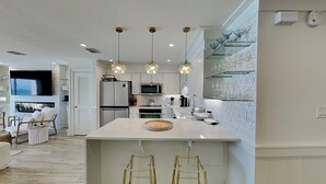 A modern kitchen with a central island, pendant lights, and a dining area with bar stools. - Dune Villas #4A (Santa Rosa Beach)