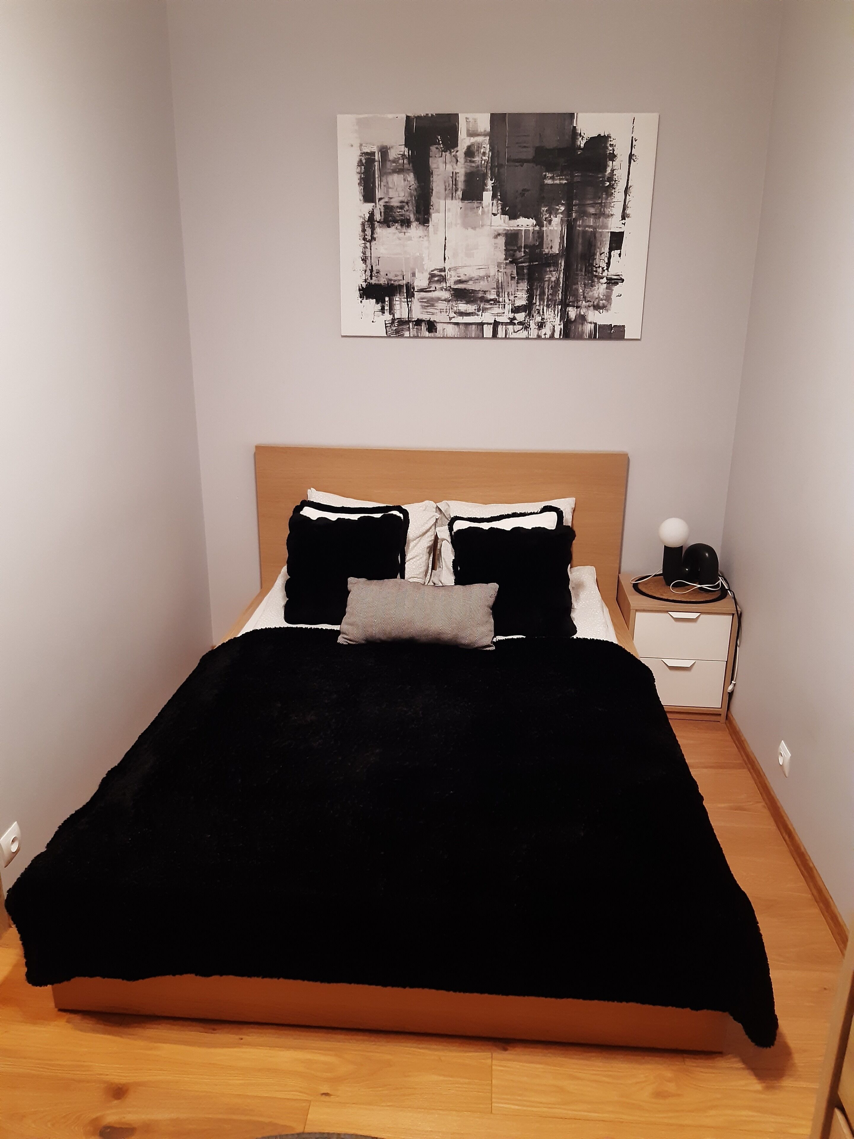 Un lit avec une tête de lit noire et blanche, une petite table de chevet avec une lampe et un tableau abstrait accroché au mur.