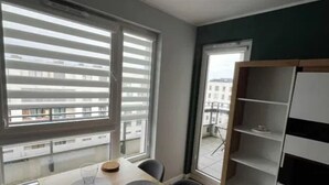A modern room with a wooden table, black chairs, a white shelving unit, and large windows with blinds.