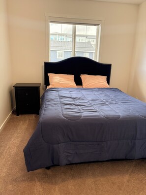 Un dormitorio con cama, mesita de noche y ventana.
