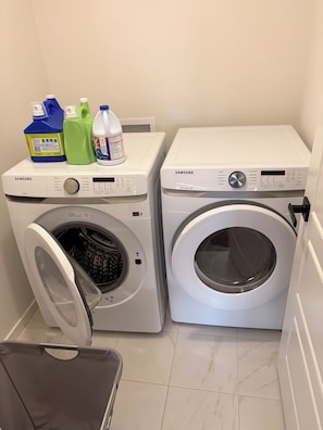 Deux machines à laver Samsung dans une buanderie, avec une valise grise posée sur le sol.