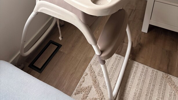A high chair with a cushioned seat and backrest, positioned in a room with a wooden floor, a white wall, and a potted plant. - Luxury 4BR Calgary Home|Families| Sleeps 8|AC& Free Parking & WiFi|Near Airport| (Calgary)