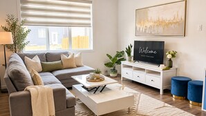 A modern living room with a sectional sofa, a coffee table, a TV on a white stand, and a decorative plant. - Luxury 4BR Calgary Home|Families| Sleeps 8|AC& Free Parking & WiFi|Near Airport| (Calgary)