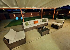 Eine Terrasse im Freien mit Korbmöbeln, einem Grill und einem grünen Rasen.