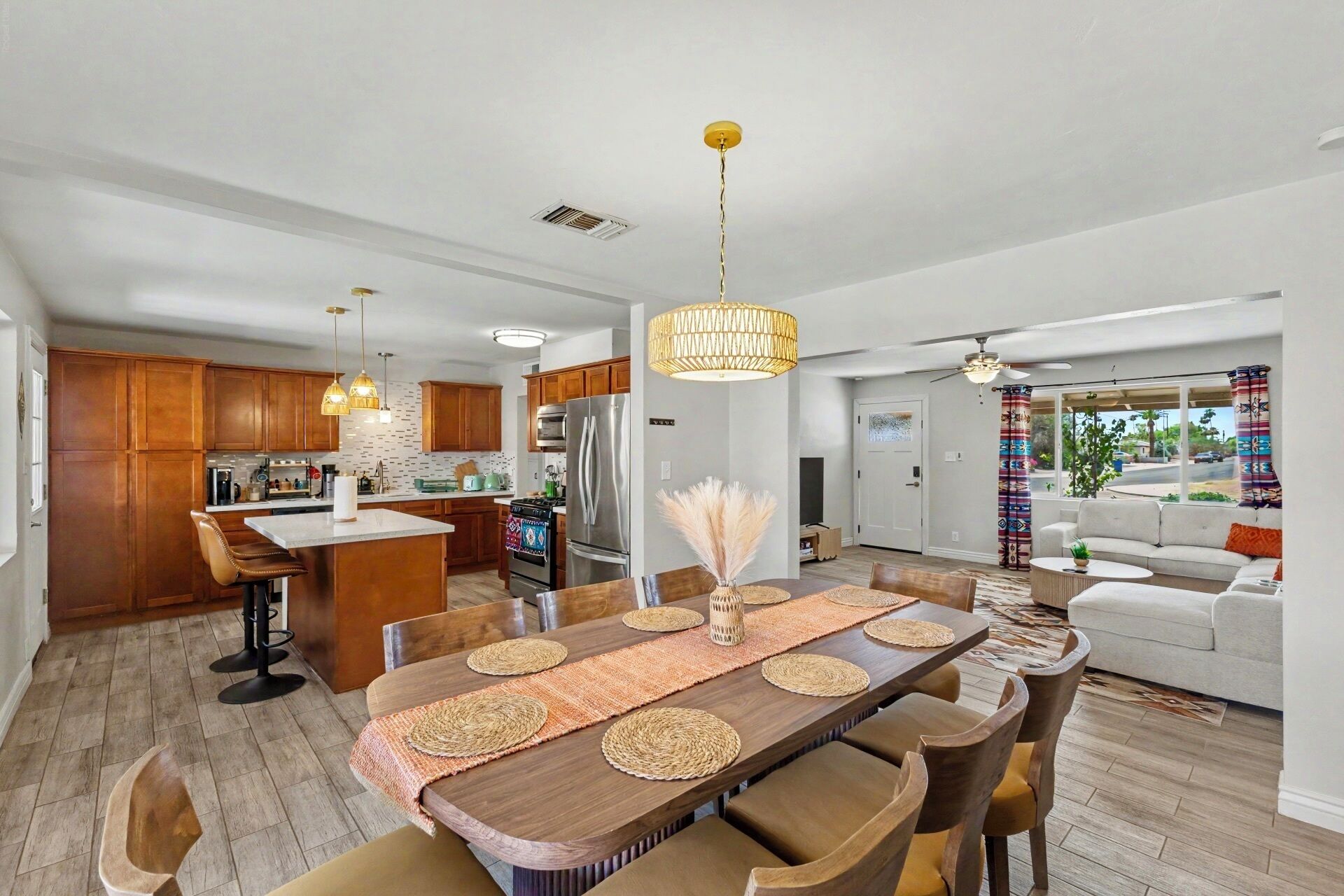 A modern kitchen with wooden cabinets, a central island, and a dining area with a large wooden table and woven placemats.