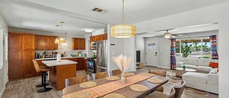 A modern kitchen with wooden cabinets, a central island, and a dining area with a large wooden table and woven placemats.
