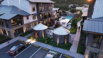 A modern multi-story building with a rooftop pool, outdoor seating, and a large cylindrical water feature.