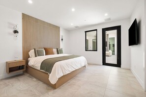Ein modernes Schlafzimmer mit einem großen Bett, Nachttischen, einem an der Wand montierten Fernseher und einer Schiebetür zu einem Badezimmer.