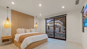 Camera da letto moderna con un letto grande, parete rivestita in legno e vista su una piscina e una casa attraverso una porta scorrevole.