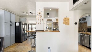 Eine moderne Küche mit grauen Schränken, einem schwarzen Kühlschrank, einer Kaffeemaschine und einem Traumfänger.