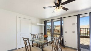 Ein Essbereich mit einem Glastisch, vier Stühlen, einem Deckenventilator und Blick auf einen Balkon.