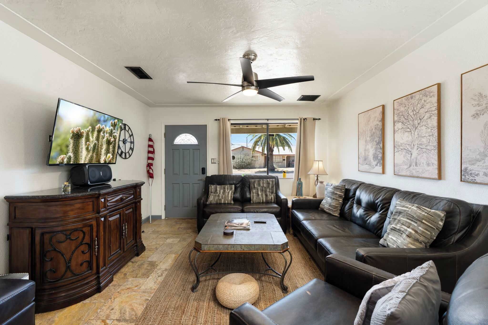 A living room with a dark leather sofa, a wooden cabinet, a television, and a ceiling fan.