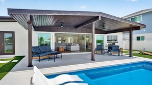 Ein moderner Poolbereich im Freien mit überdachter Terrasse, Liegestühlen und Blick ins Haus.