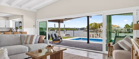 A spacious living area with a large sliding glass door leading to a pool, a ceiling fan, and a view of the water.