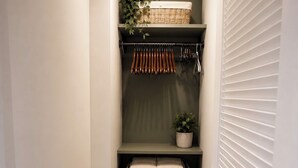A narrow hallway with a wooden floor, a green shelf with storage boxes, a hanging rack with tools, and a door with horizontal blinds. - Cozy 1-bedroom studio in welcoming North Miami Beach with AC (North Miami Beach)
