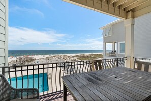 A wooden deck with a pool, overlooking a beach with umbrellas and a clear sky. - Dixie Tide - Hammock Dunes West (Orange Beach)