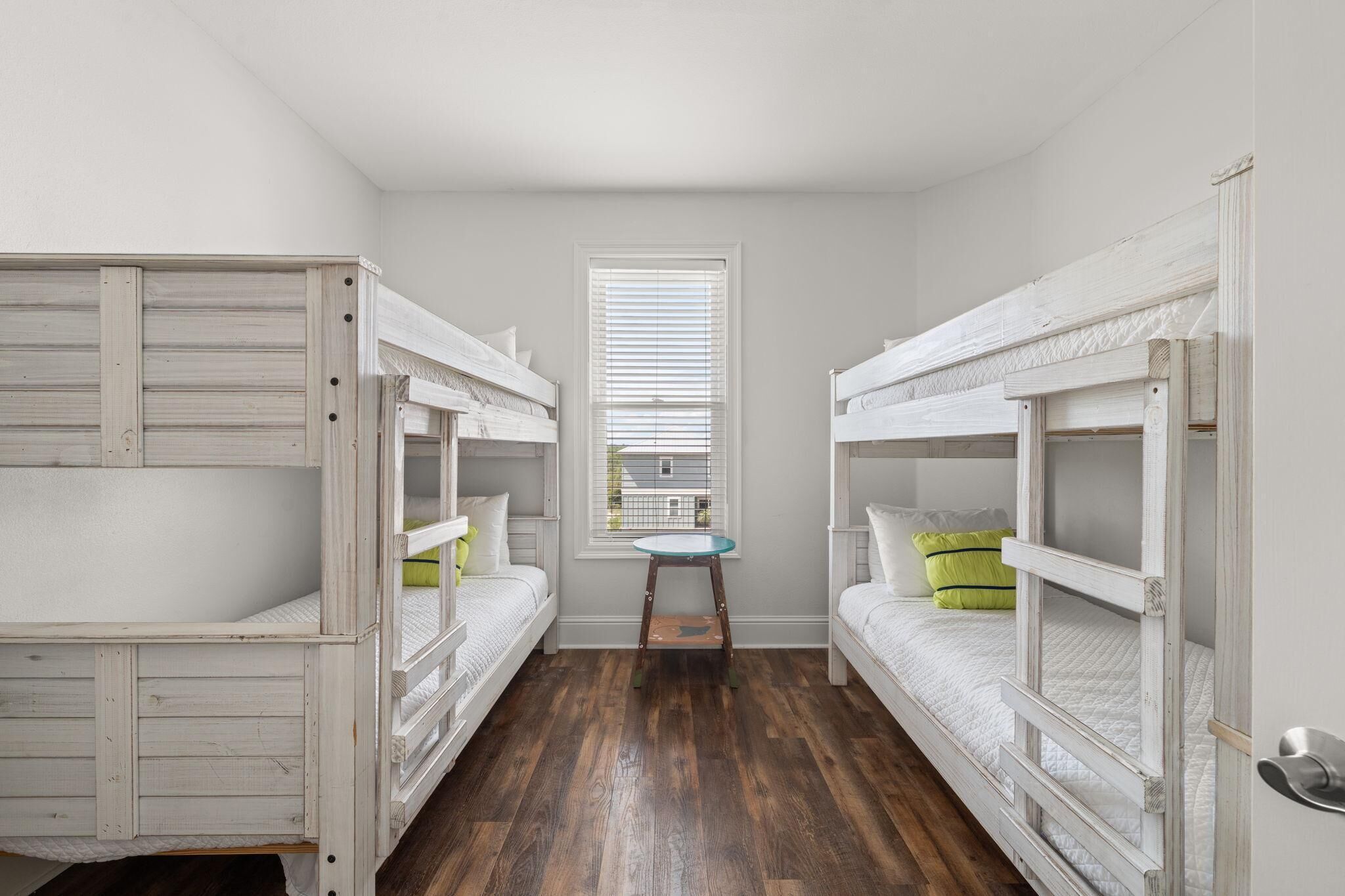 A room with bunk beds, a small table, and a window with blinds.
