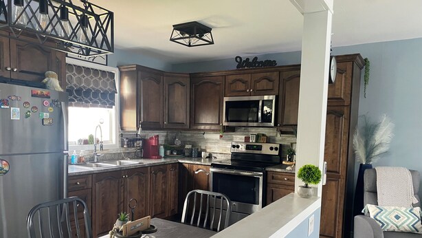 A modern kitchen with wooden cabinets, a stainless steel refrigerator, a microwave, and a dining area with a table and chairs.