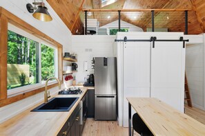 Una cocina compacta con un lavamanos, refrigerador de acero inoxidable y una mesa de madera.