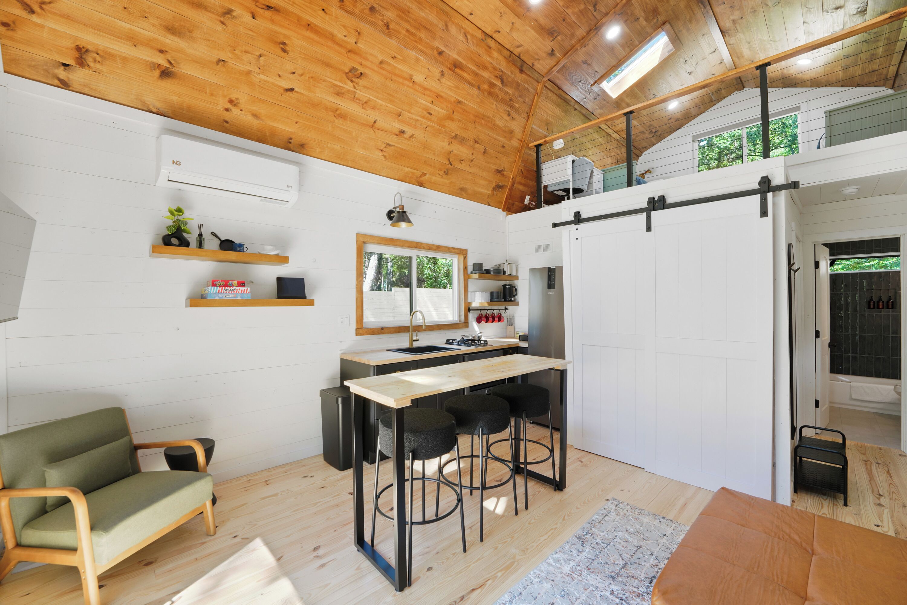 Een compacte keuken met een houten plafond, een eethoek met krukken, een bank en een klein zithoekje.