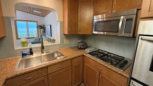Una cocina con armarios de madera, un lavaplatos de acero inoxidable, una estufa a gas, un microondas y un tostador.