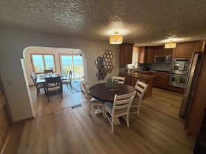 A kitchen with wooden cabinets, a dining table with chairs, and a view through a sliding door to the outside. - Spacious Lakeview Retreat Built for Relaxation & Longer Stays (Lorain)