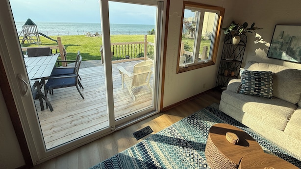 Una habitación con una puerta corrediza de vidrio que da a una terraza con mobiliario exterior, un sofá con cojines estampados y un cuadro en la pared.