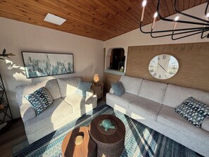 A living room with a sofa, a round wooden coffee table, a wall clock, and a framed cityscape painting. - Spacious Lakeview Retreat Built for Relaxation & Longer Stays (Lorain)