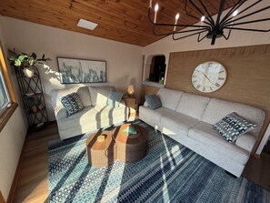 A cozy living room with a sofa, a round coffee table, a large wall clock, and a cityscape painting. - Spacious Lakeview Retreat Built for Relaxation & Longer Stays (Lorain)