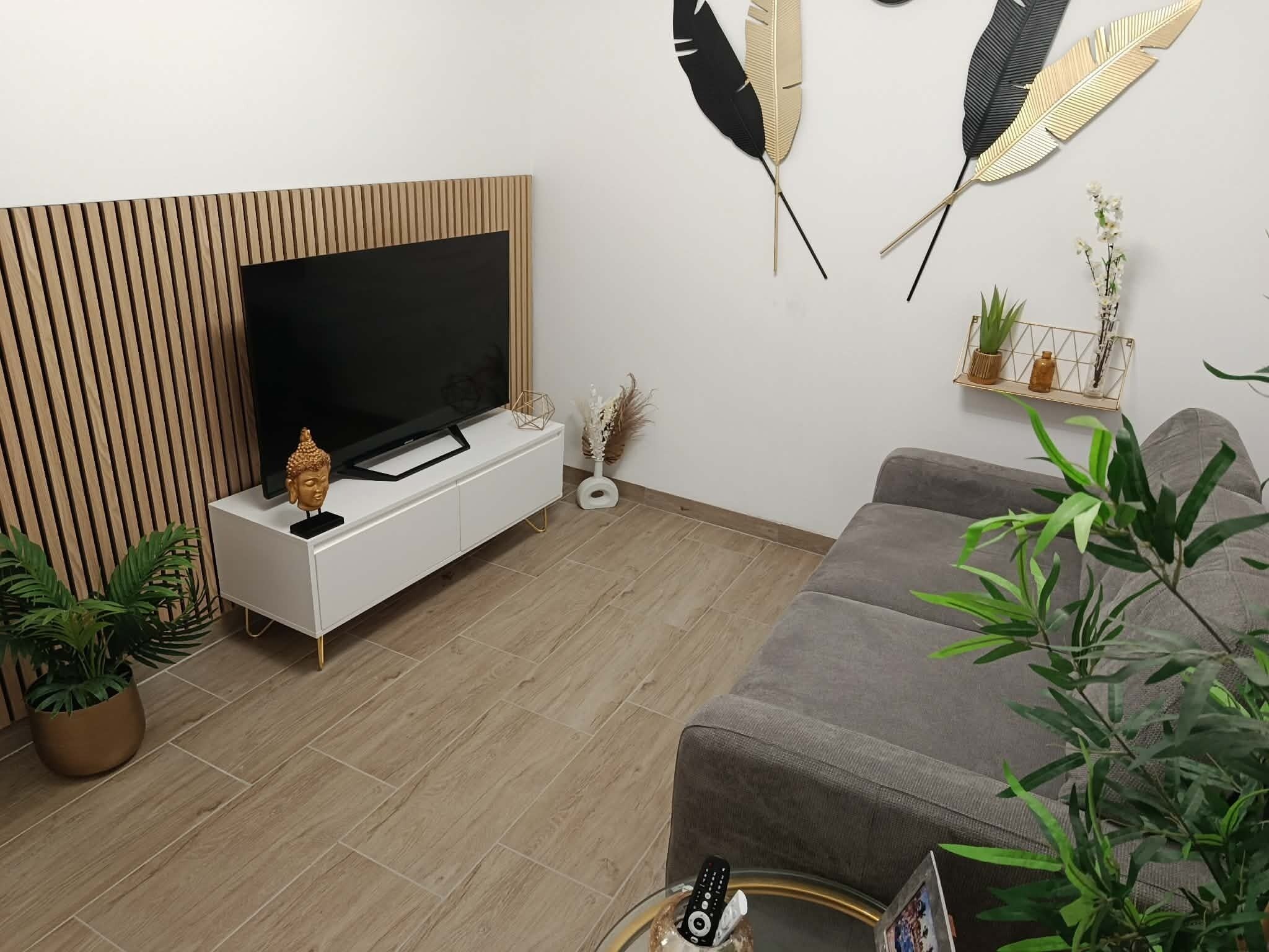 Un salon moderne avec un téléviseur à écran plat posé sur une console blanche, un canapé gris et une petite table d’appoint avec une télécommande.