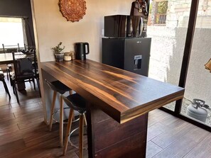 Eine moderne Küche mit einer Holztischinsel, Barhocker, einer Kaffeemaschine und einem Kühlschrank.