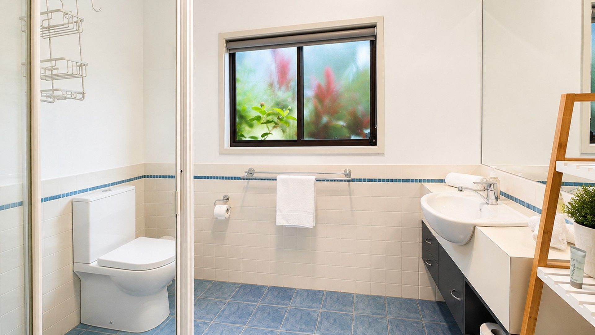 A bathroom with a toilet, sink, and window with a view of greenery.