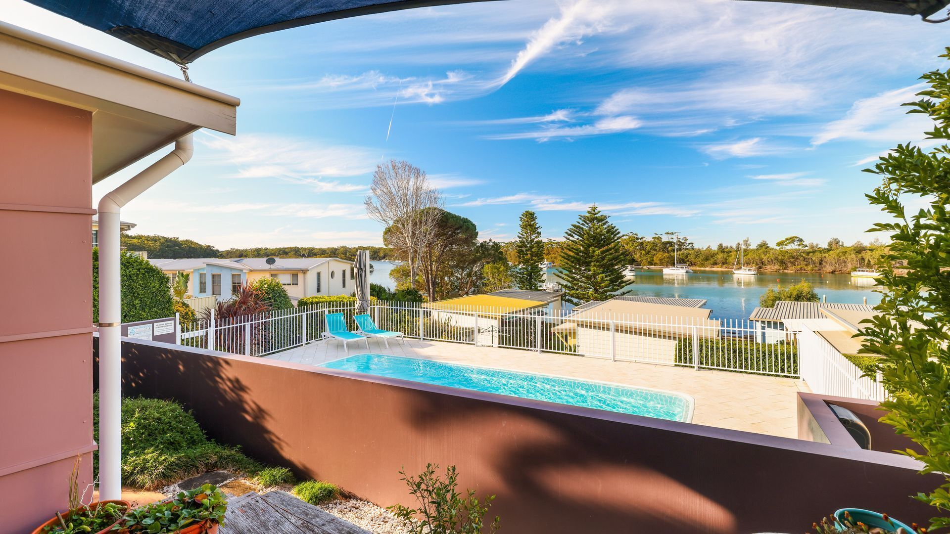 A swimming pool with a view of a lake and boats, surrounded by a fence and greenery.