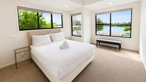 A bedroom with a large bed, two windows, a bench, and a view of a body of water. - Anglesea Family Bungalow Pool View by Book Jervis Bay (Huskisson)