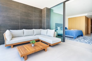 Ein modernes Zimmer mit einer Eckcouch, einem Holztisch und einem Bett mit blauer Bettdecke.