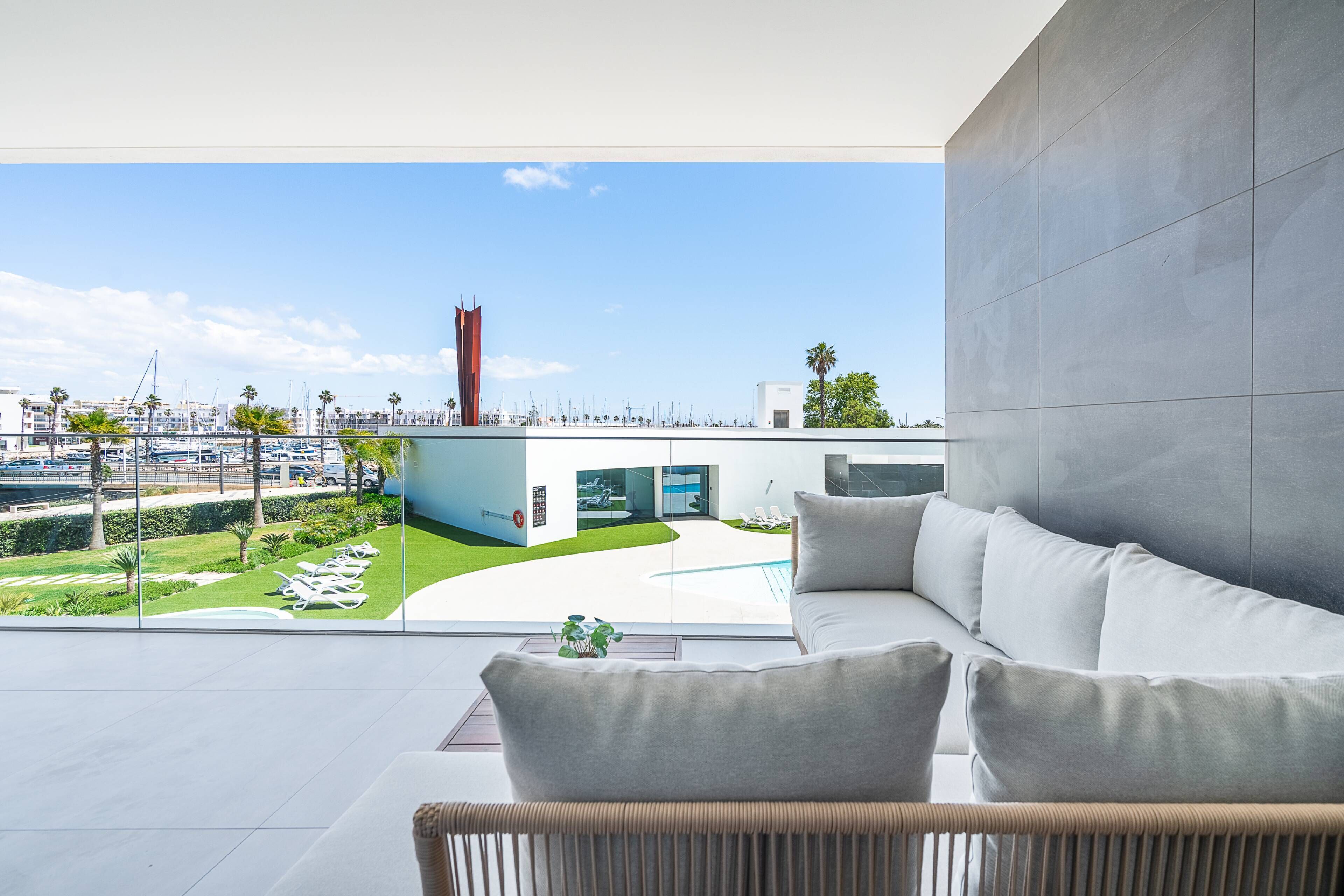 Un interior moderno con vista a un puerto deportivo, un sofá blanco y una pared de cristal.