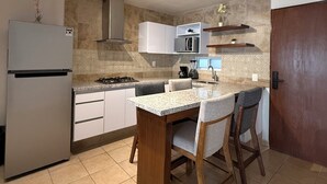 Eine kompakte Küche mit Kühlschrank, Herd, Mikrowelle und einer kleinen Essecke mit Stühlen.
